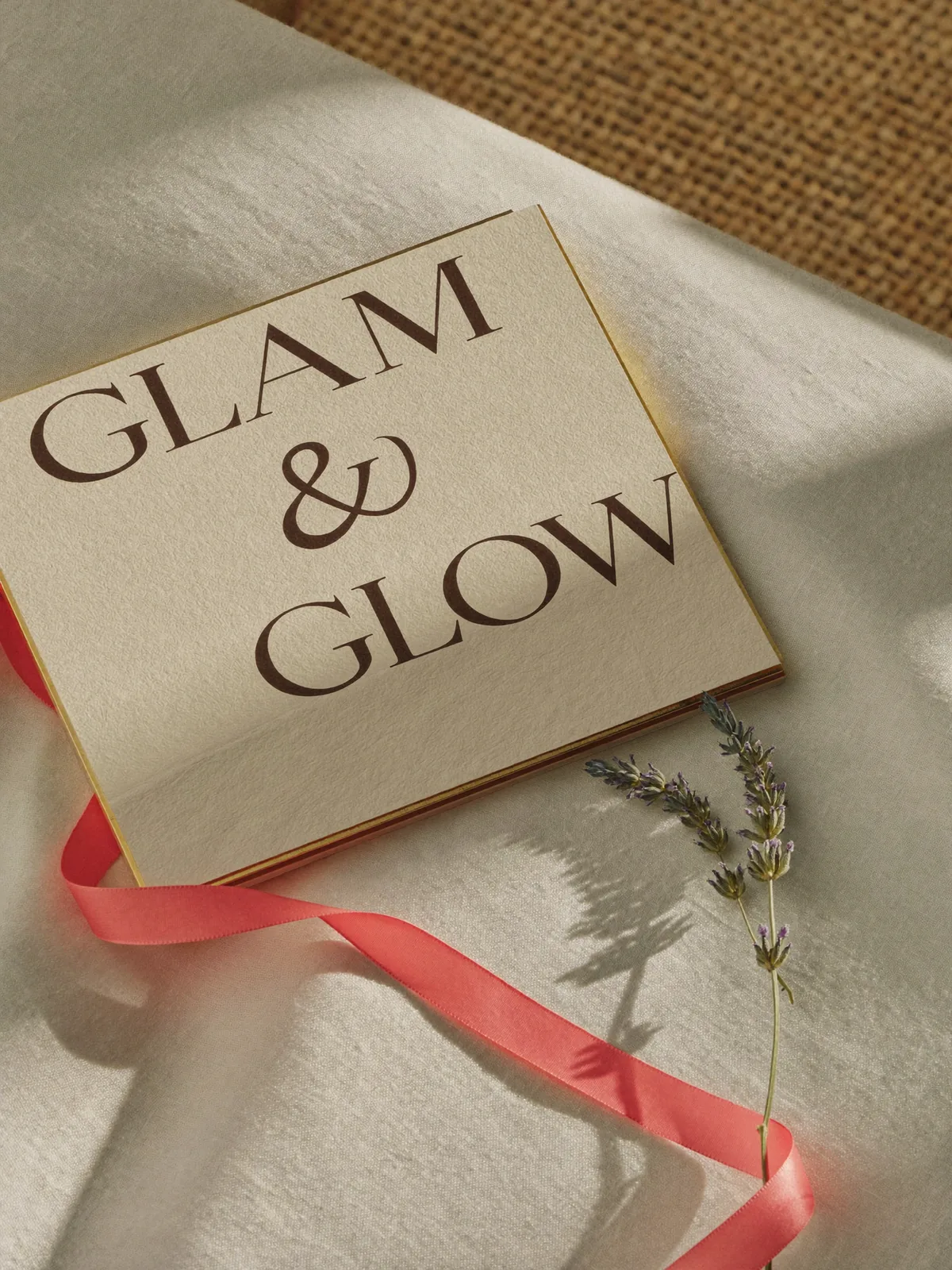 Editorial photograph of a Glam & Glow gift voucher card on cream linen with silk coral ribbon